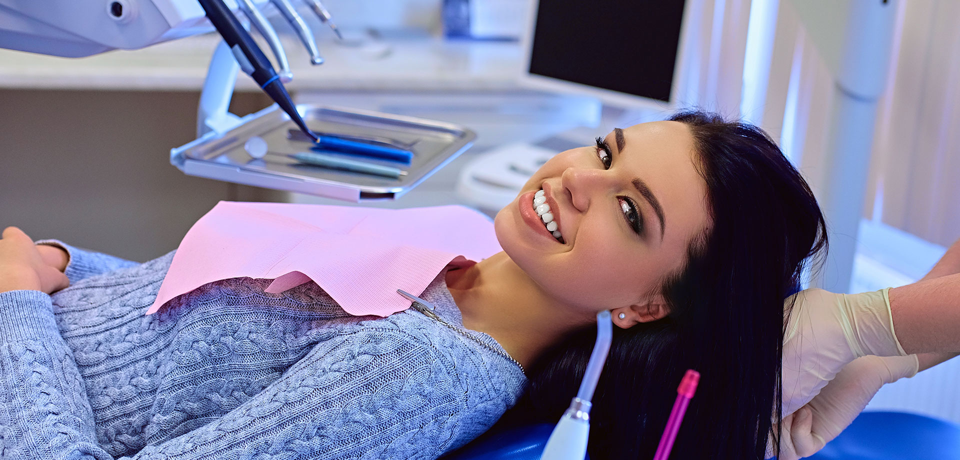 A woman sitting in a dental chair, smiling at the camera, with her teeth being worked on.