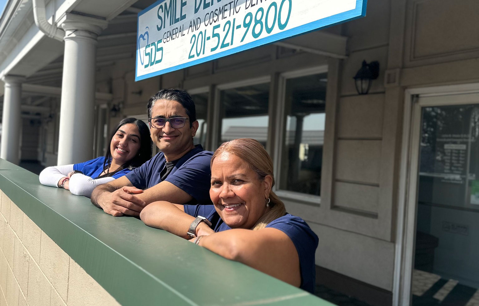 Three individuals posing in front of a building with a sign that reads  SMILE WELLNESS CENTER.