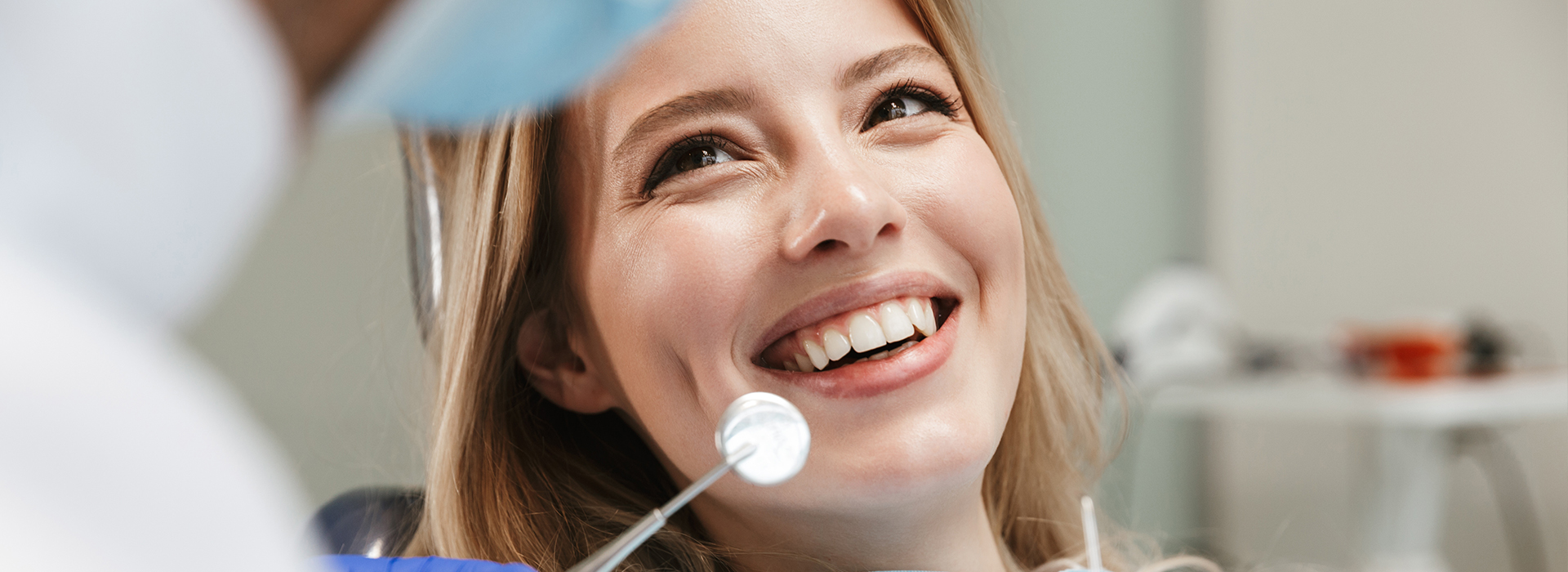 The image shows a woman with a broad smile, sitting in a dental chair during a dental appointment.