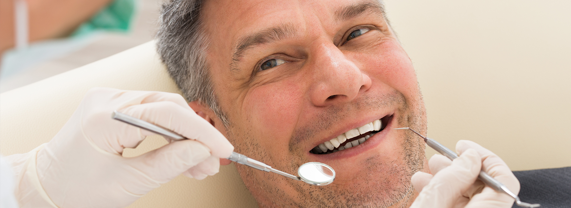 A man sitting in a dental chair receiving a dental treatment, with a smiling expression and a dental professional working on his teeth.